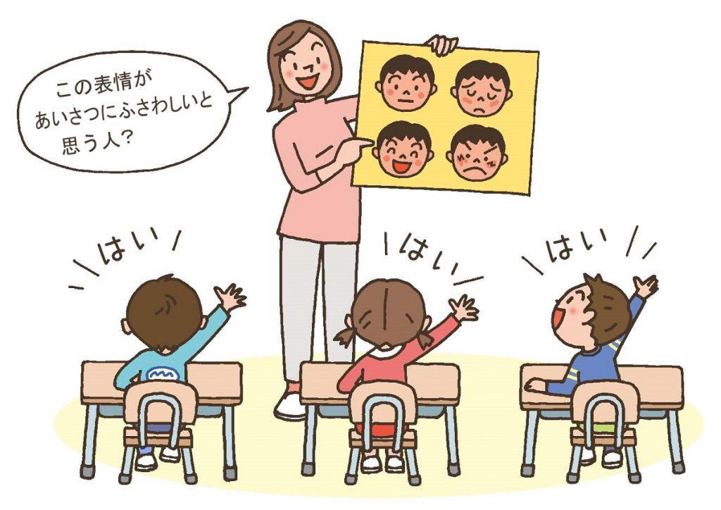 あいさつの仕方のソーシャルスキルトレーニングで、あいさつクイズを出す教師。にこやかな表情をしたイラストを指差し、「この表情があいさつにふさわしいか」を聞いていてる。子供たちは挙手で意思表示している。