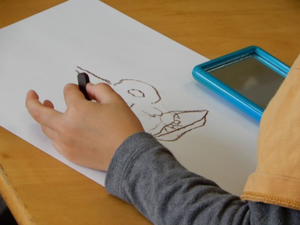 「非利き手自画像」に取り組む子供。左手でコンテを持って、書き始める。