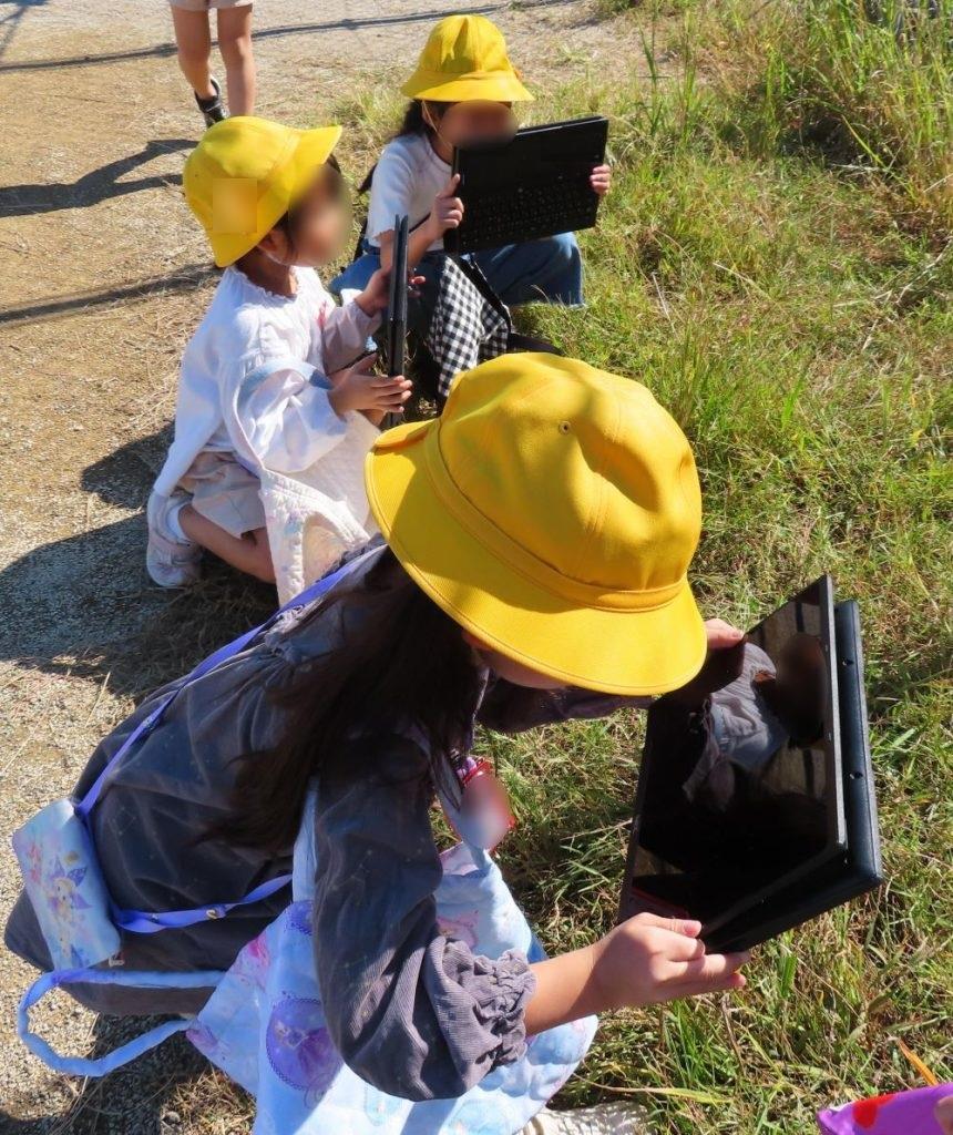 校外に出て秋みつけをする子供たち。見つけた秋をタブレットで撮影している