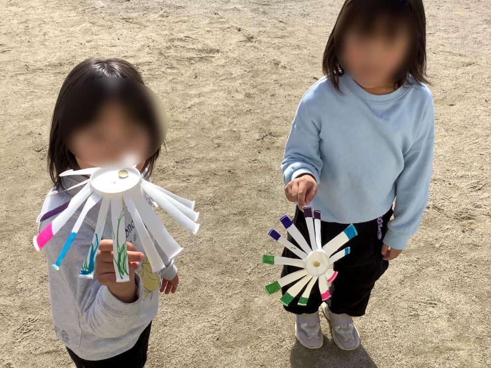 紙コップで作った風車で遊んでいる子供。