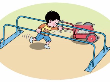 手押しの二輪車で砂を運んでいる男の子が、鉄の棒が２本ある遊具の下をくぐって移動しようとしている。