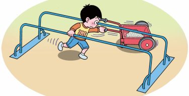 手押しの二輪車で砂を運んでいる男の子が、鉄の棒が２本ある遊具の下をくぐって移動しようとしている。