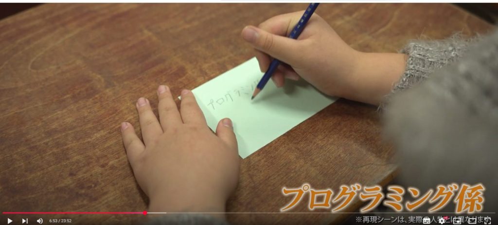 研修用動画の一場面。投票用紙に「プログラミング係」と書く場面