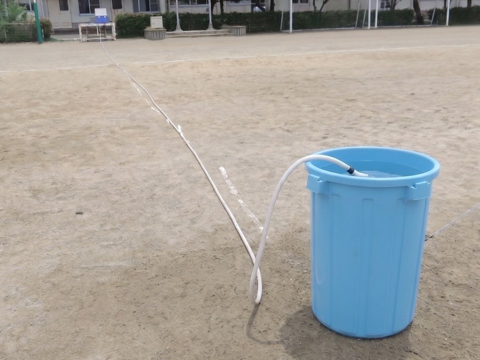 手洗い場の蛇口からホースリールでグラウンドのポリバケツに水を溜める。